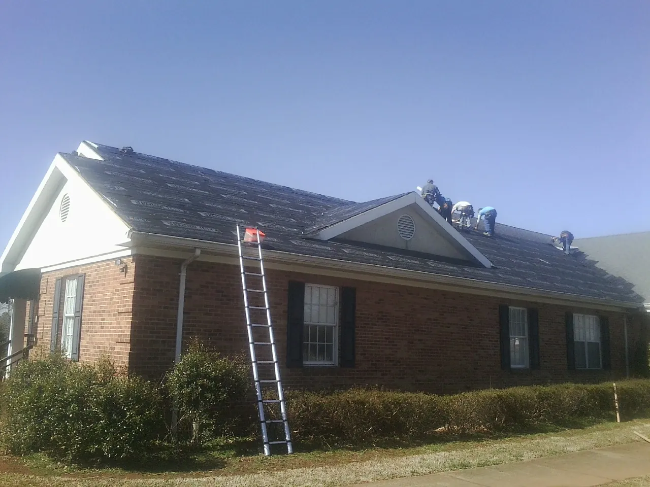 Crew tearing shingles off a brick ranch roof with a ladder set — Emergency Roof Repair work by our crew in Pequea