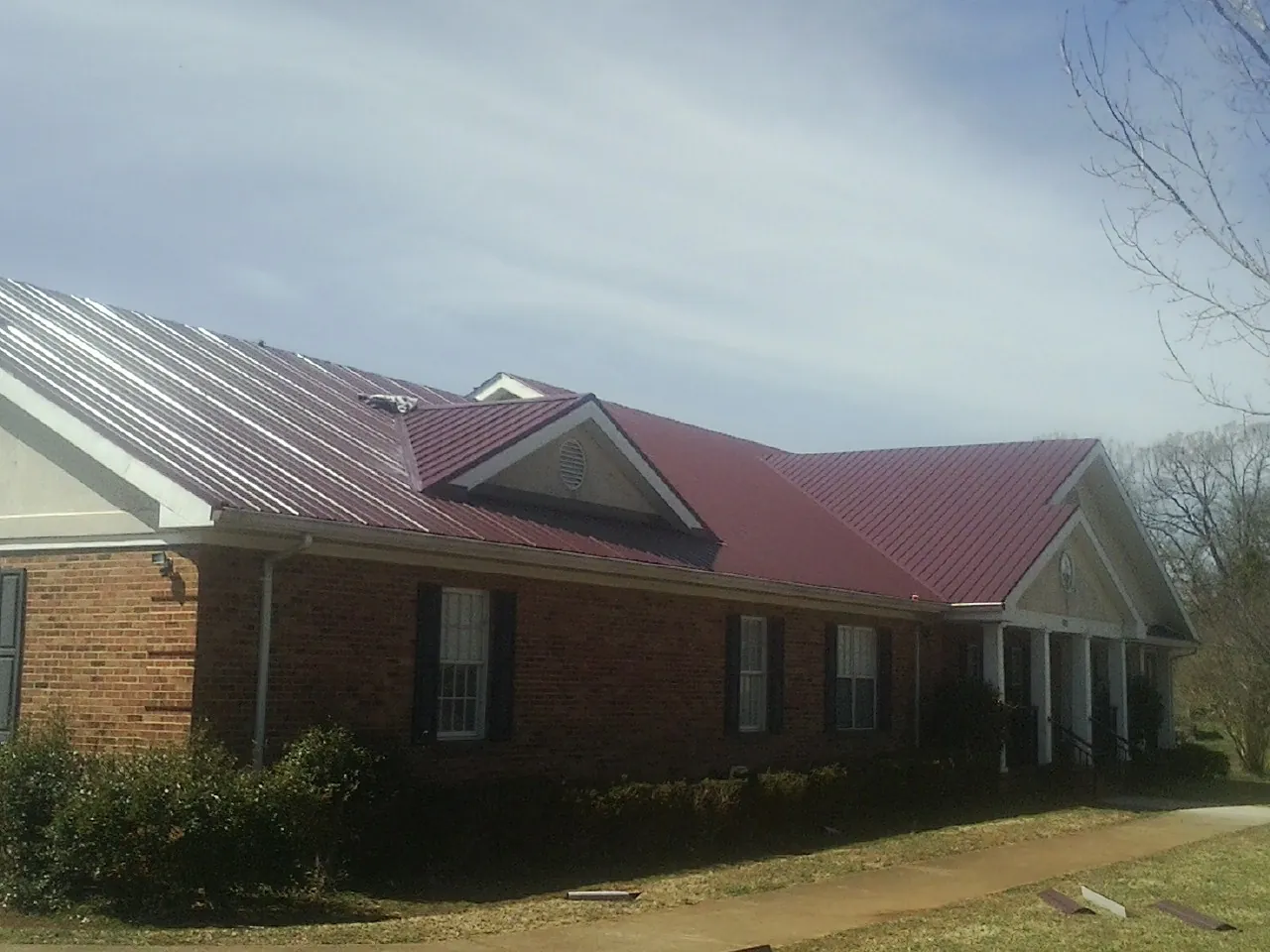 Red metal roof with gabled entries on a long brick building, from a Hail Damage Roof Repair job in Pequea