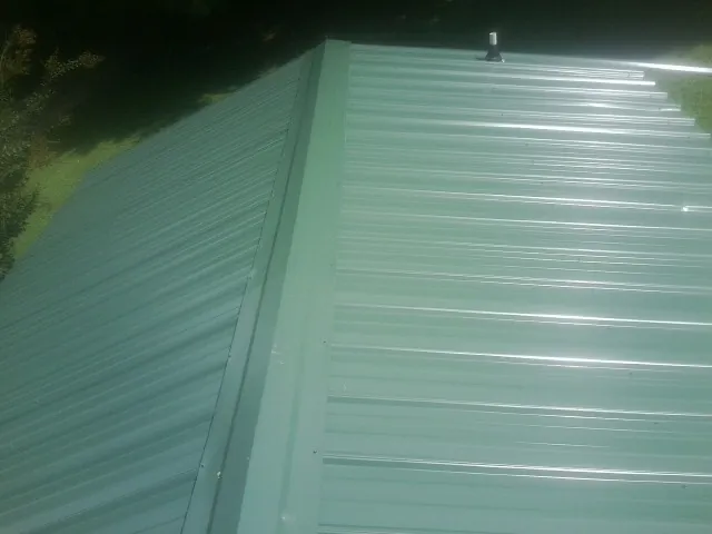 New green metal panels meeting at the ridge of a roof — Flat Roof Repair work by our crew in Pequea