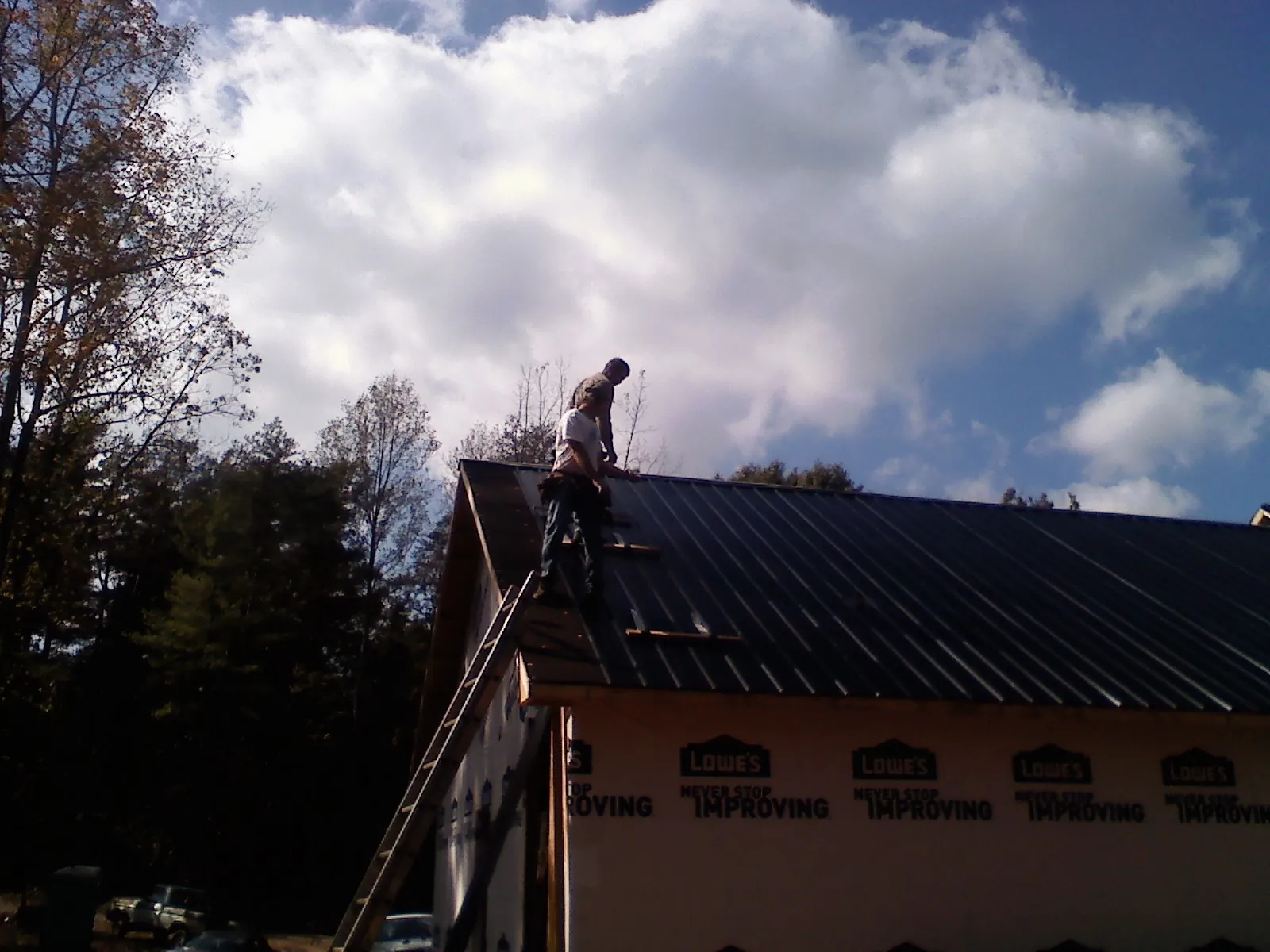 Roofer fastening dark metal panels high against a cloudy sky, from a Roof Inspection job in Pequea